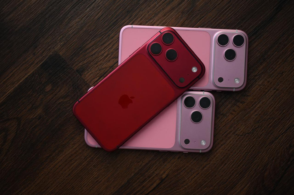 Three smartphones in red, pink, and purple on a wooden surface