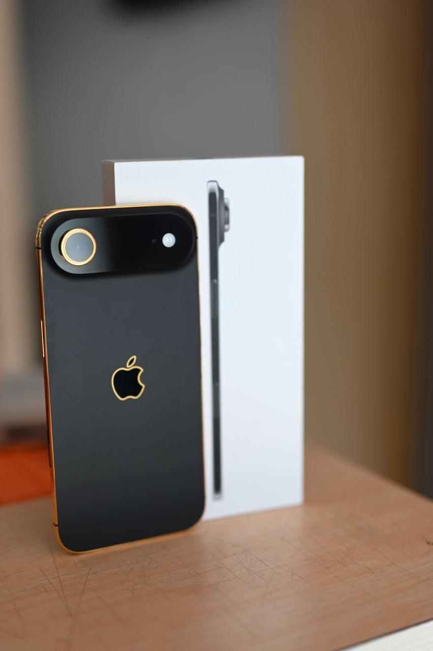 Black smartphone with gold accents on a wooden surface, with a blurred background