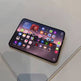 A black smartphone with a large colorful display showing various app icons, resting on a glossy, light-colored glass surface.
